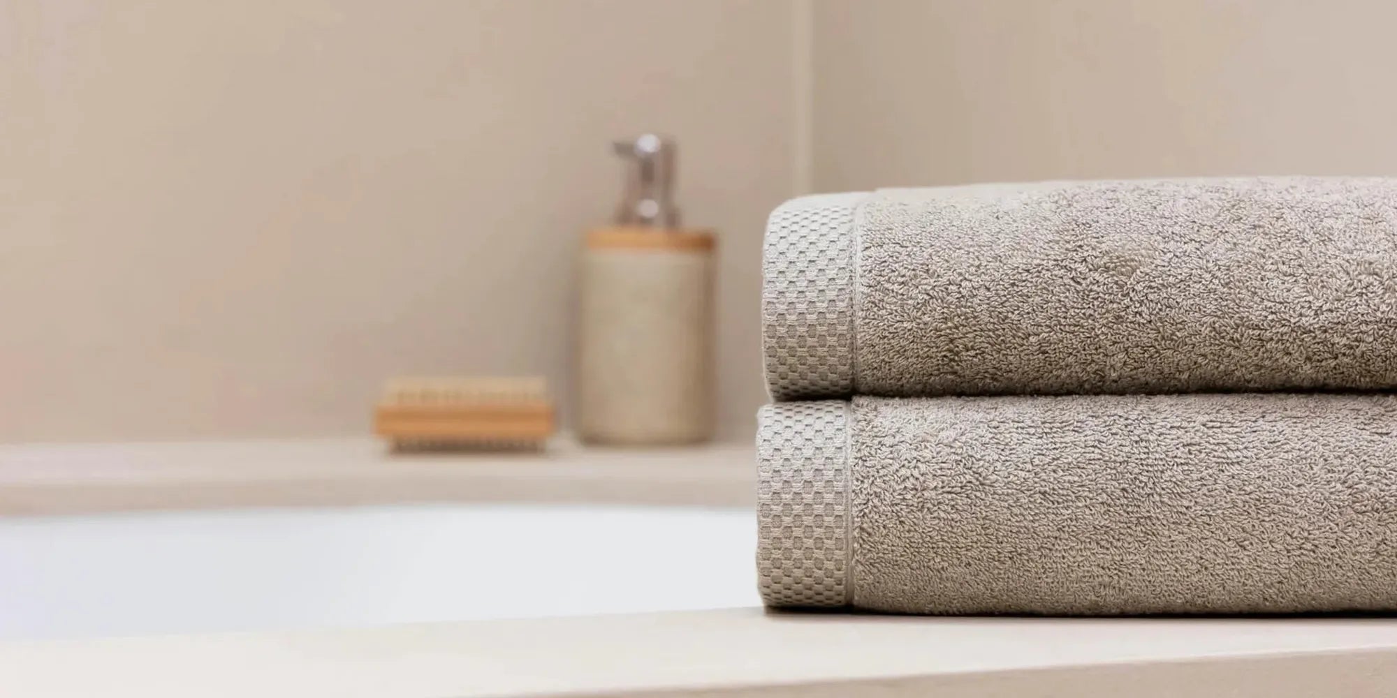 Twee luxe latte handdoeken in stijlvolle badkamer met zeeppompje op de achtergrond